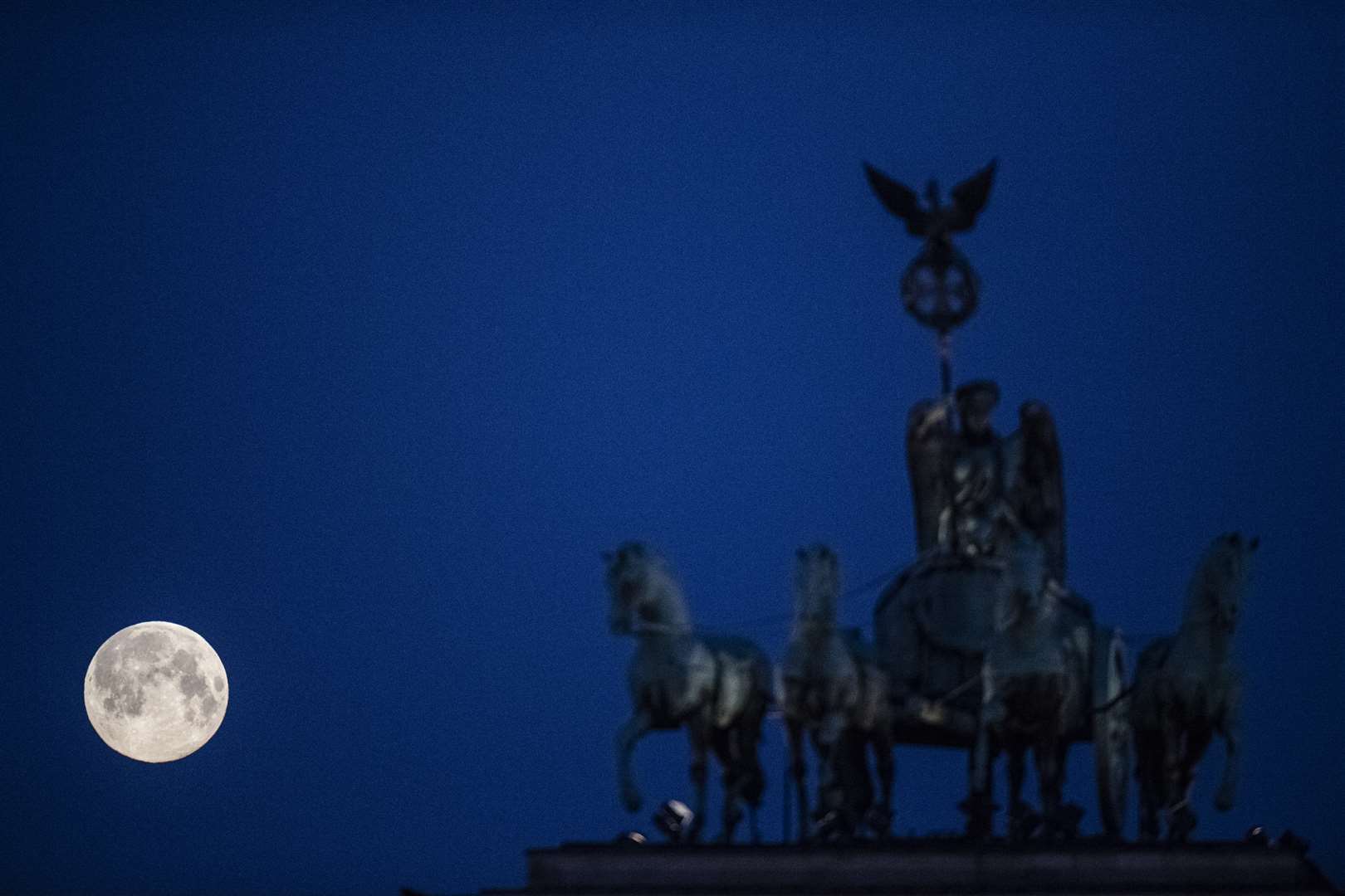 The supermoon sets behind the Brandenburg Gate in Berlin (Paul Zinken/dpa via AP)