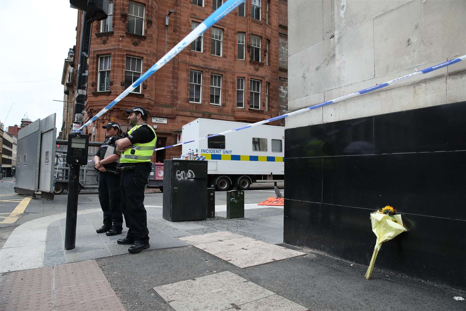 Police, alongside a floral tribute, at the scene in West George Street, Glasgow (PA/Andrew Milligan)