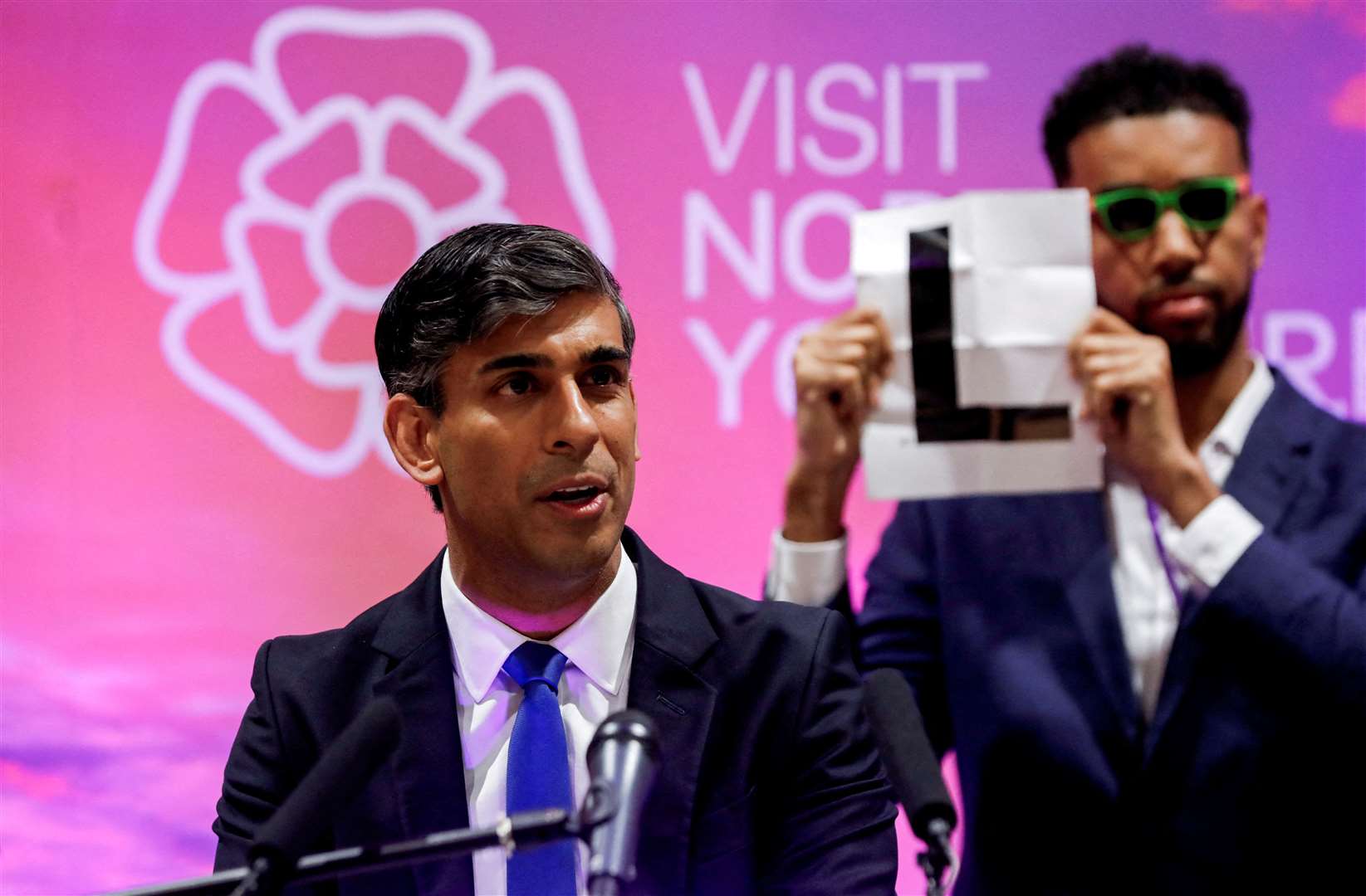 Independent candidate Niko Omilana holds an L behind Rishi Sunak during his speech at Northallerton Leisure Centre (Temilade Adelaja/PA)