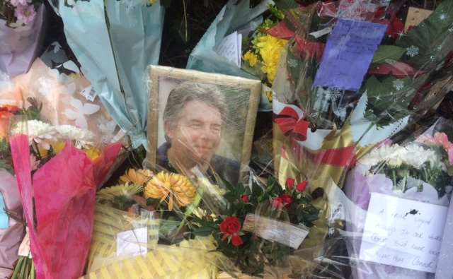 A photo sits between bouquets of floral tributes left at the scene of the fatal crash in Ash Road, New Ash Green