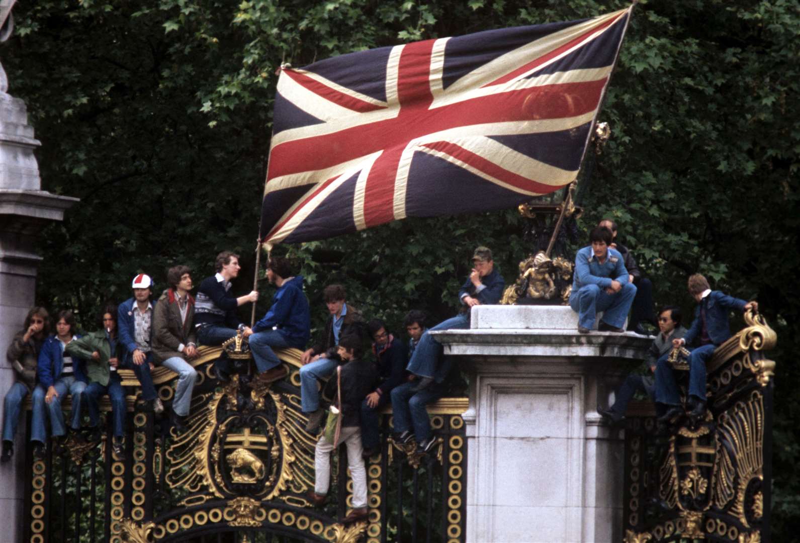 Flag-waving spectators find a vantage point outside Buckingham Palace to watch the royal procession for the special Silver Jubilee service of thanksgiving (PA)