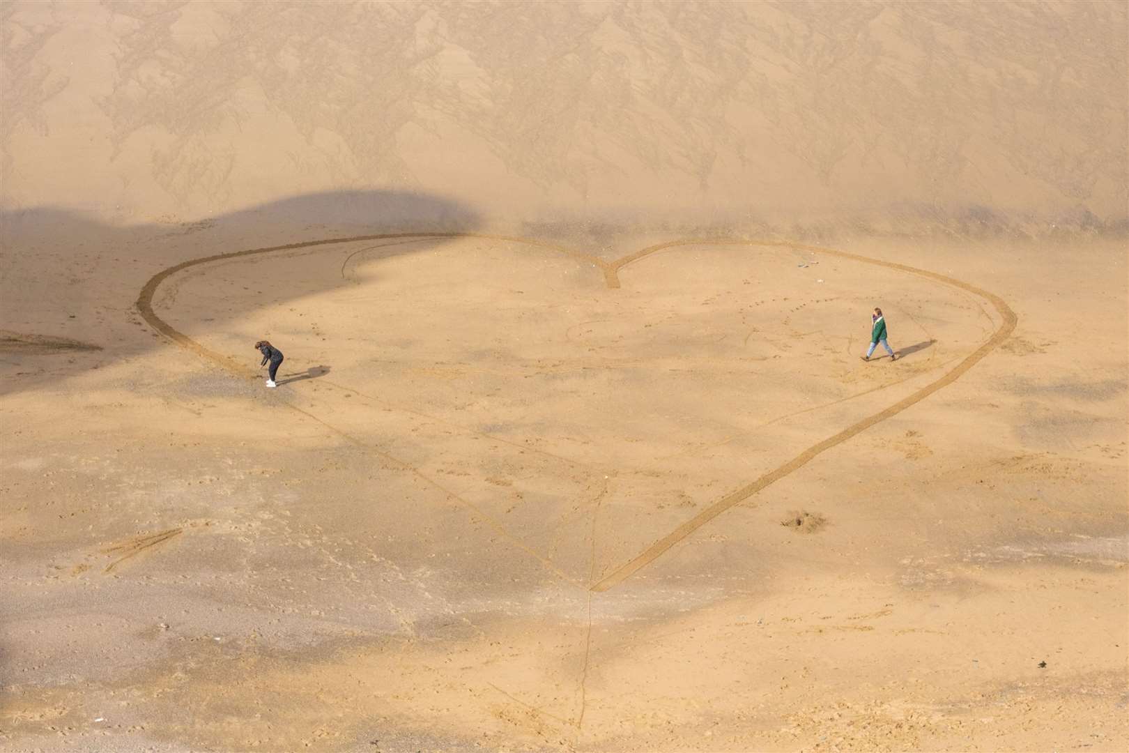 People draw a heart in the sand on the beach at Newquay, Cornwall (PA)