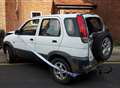 Battered car with smashed-out window dumped on road