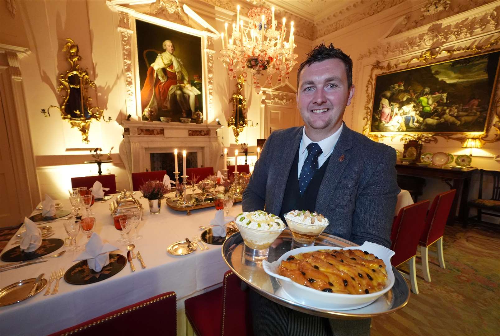 Evan Samson, who leads the front of house team, with a lemon and pistachio syllabub, bread and butter pudding alongside an apple and almond trifle in the Pink Dining Room (Andrew Milligan/PA)