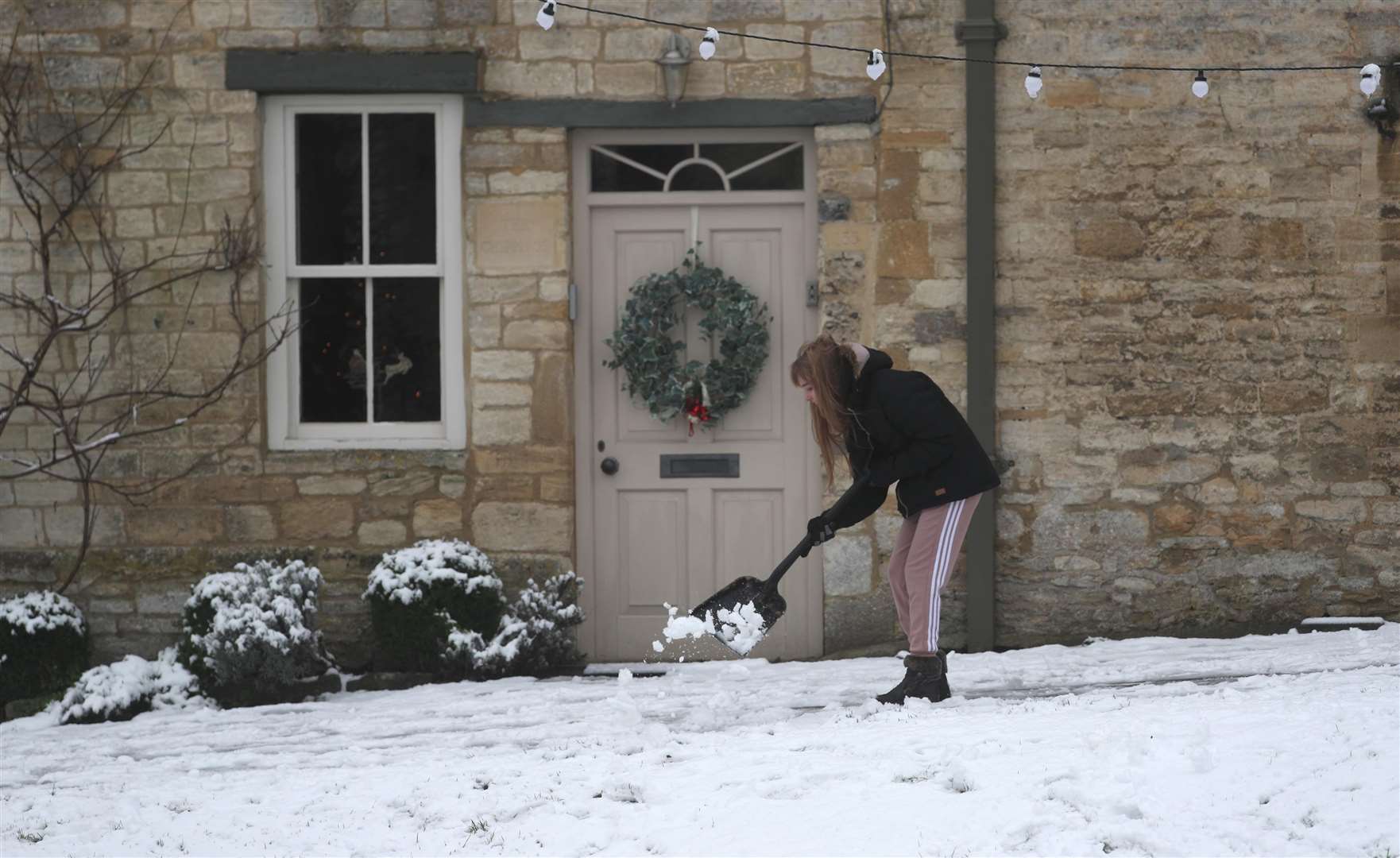 A woman clears snow from pathways in Burford, West Oxfordshire (Steve Parsons/PA)