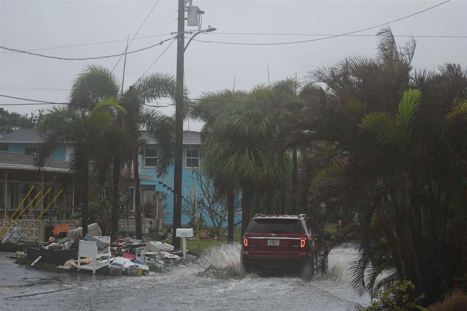 A car drives past a pile of debris from Hurricane Helene flooding, along a street that had already begun flooding from rain ahead of the arrival of Hurricane Milton, in Gulfport, Florida (Rebecca Blackwell/AP)