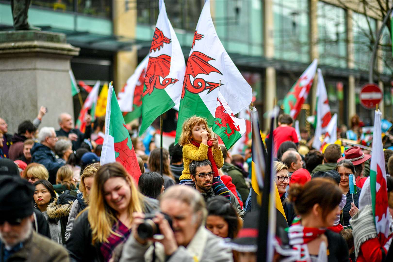 Members of the public wave flags as they gather to watch a St David’s Day Parade in Cardiff (Ben Birchall/PA)