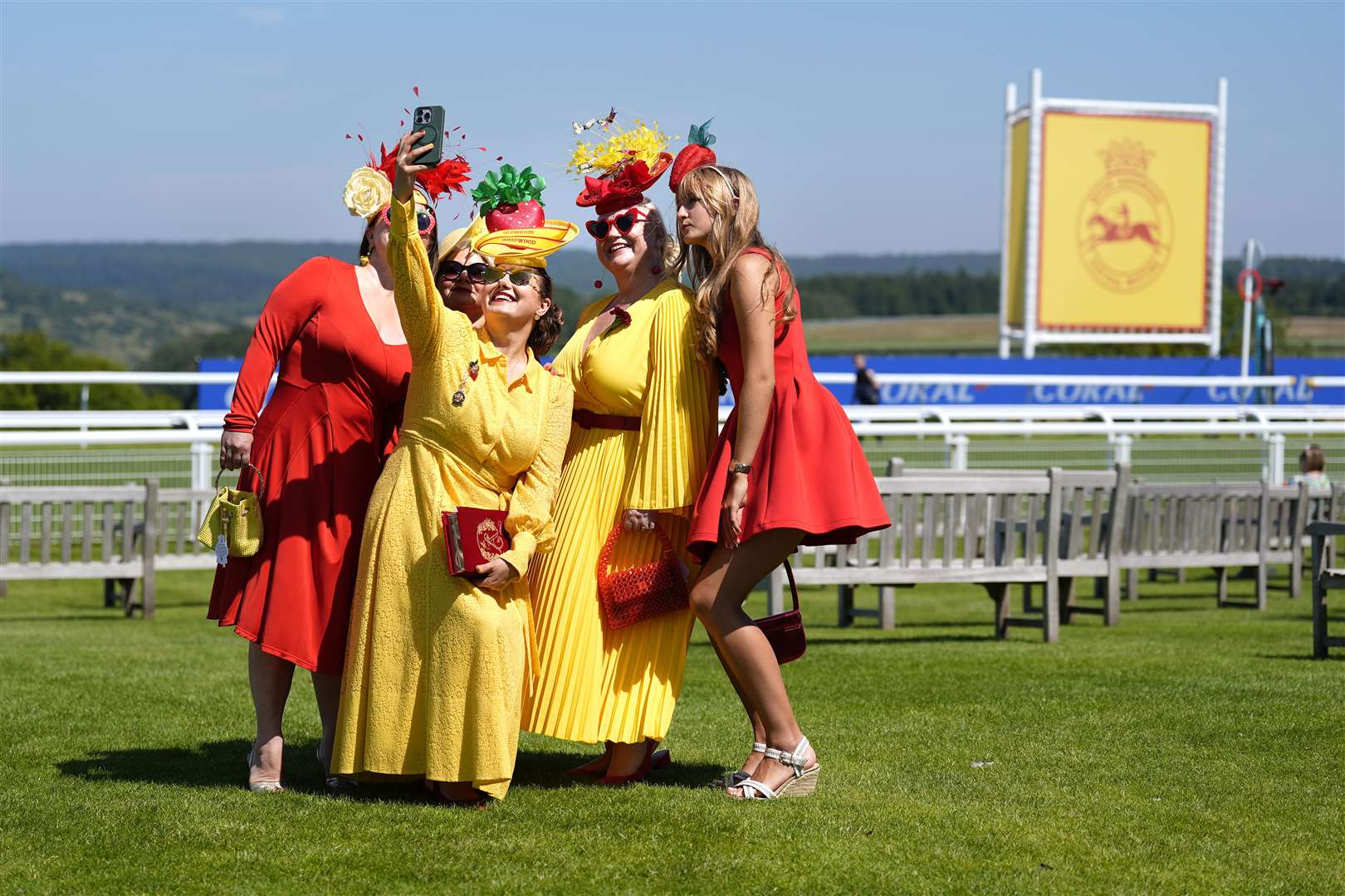 Racegoers in red and yellow dresses take photographs during day one of the Qatar Goodwood Festival at Goodwood Racecourse in Chichester (Andrew Matthews/PA)