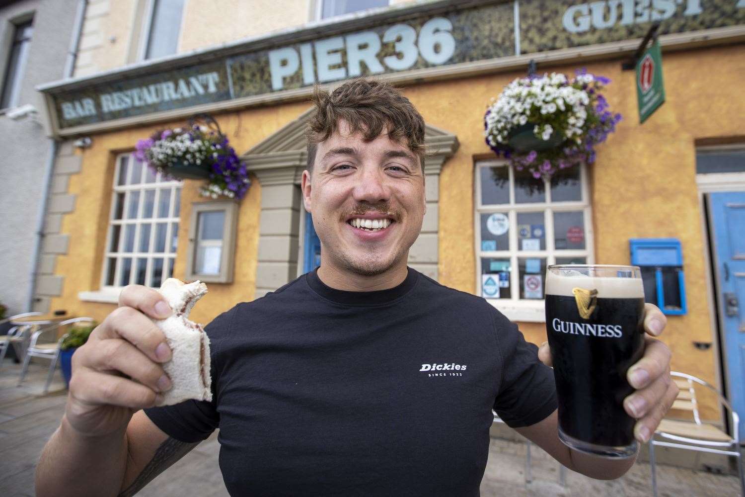 Jordan Leckey holding a celebrity jam sandwich and pint of Guinness outside Pier 36 at Donaghadee Harbour in Northern Ireland after his record swim (Liam McBurney/PA)