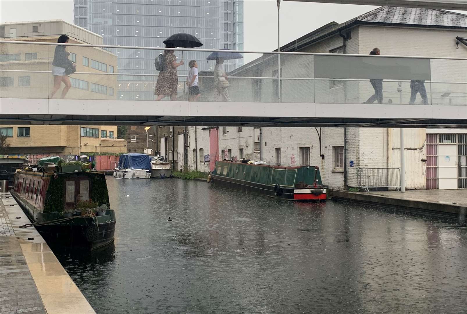 Commuters shelter beneath umbrellas while crossing a bridge over the canal in Paddington, west London (Peter Clifton/PA)