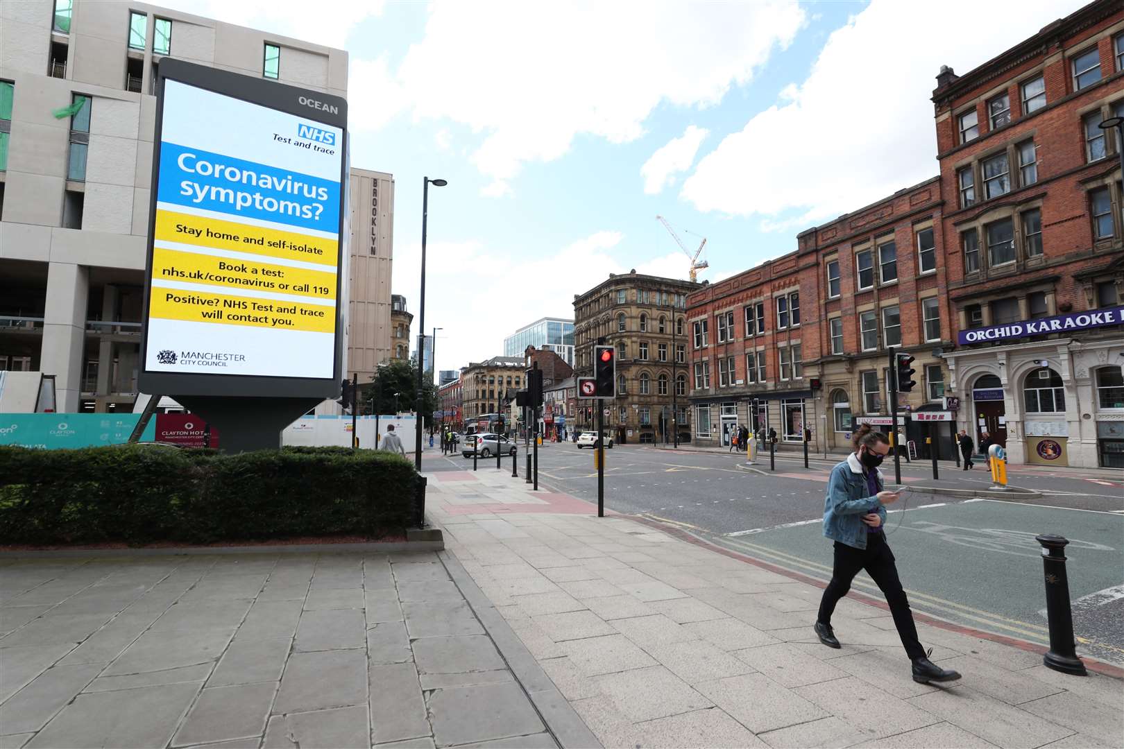 A person wearing a mask walks past coronavirus advertising in Manchester (Peter Byrne/PA)