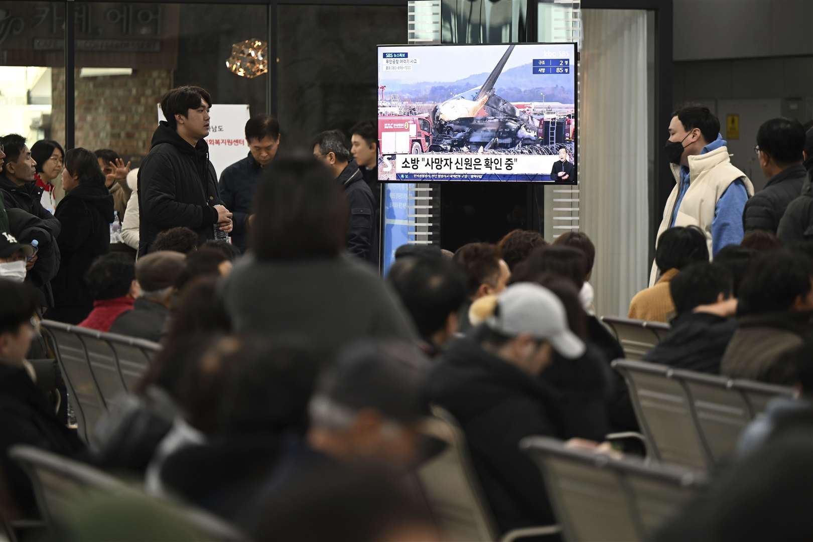 Family members of the passengers on a plane which burst into flames watch a TV news programme at Muan International Airport (Park Ki-woong/Newsis via AP/PA)