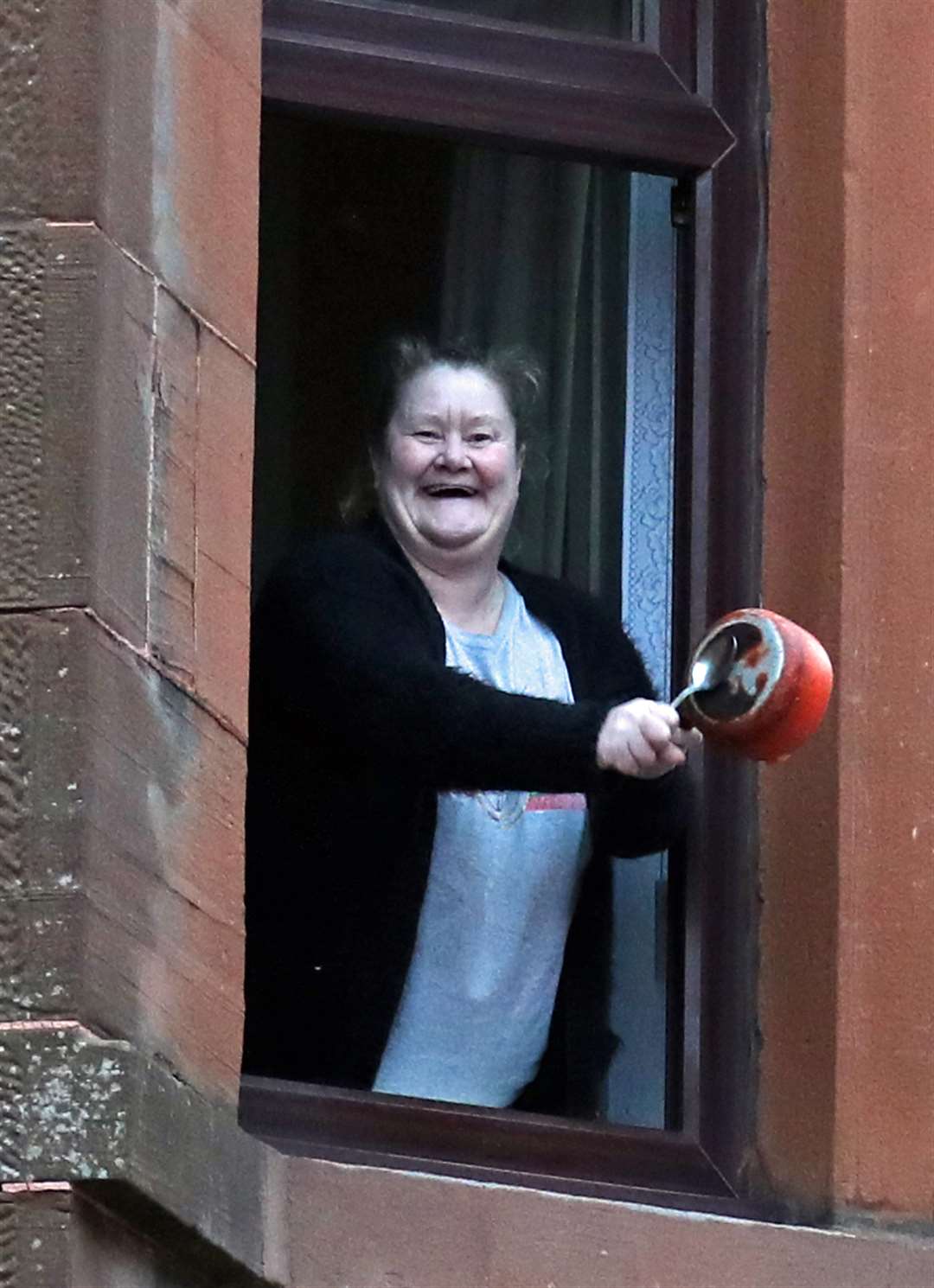 A woman bangs a saucepan from her flat window in Glasgow (Andrew Milligan/PA)