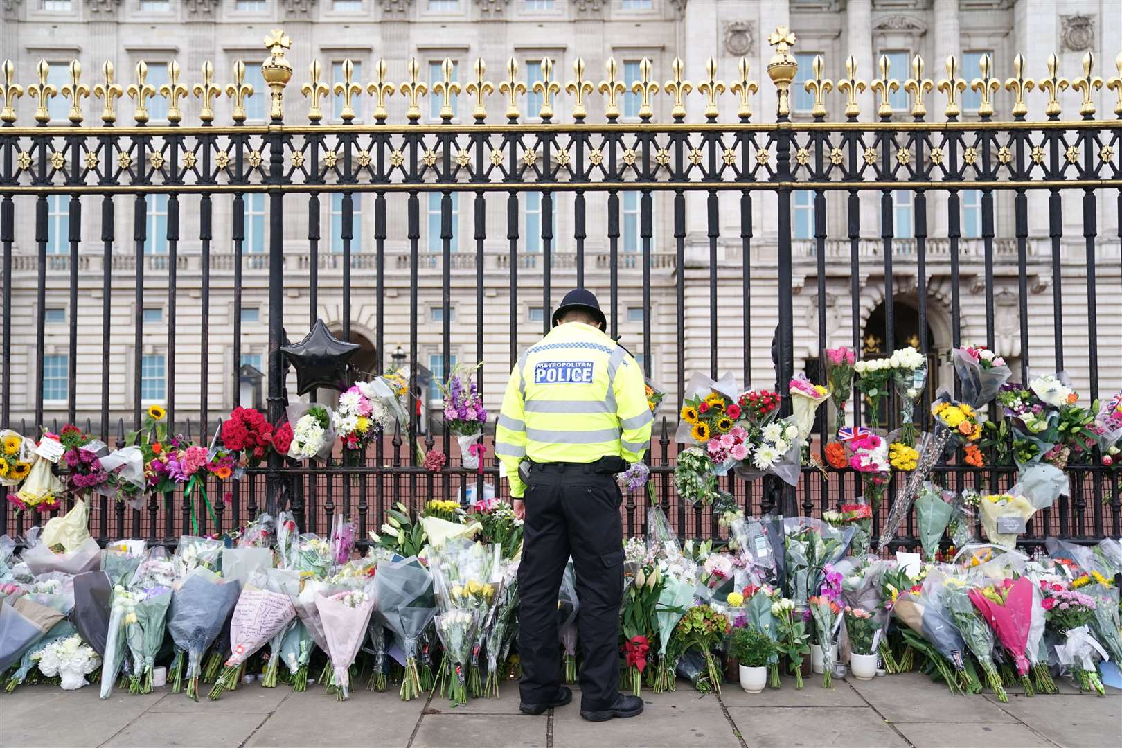 A police officer looks at flowers laid outside Buckingham Palace (Kirsty O’Connor/PA)