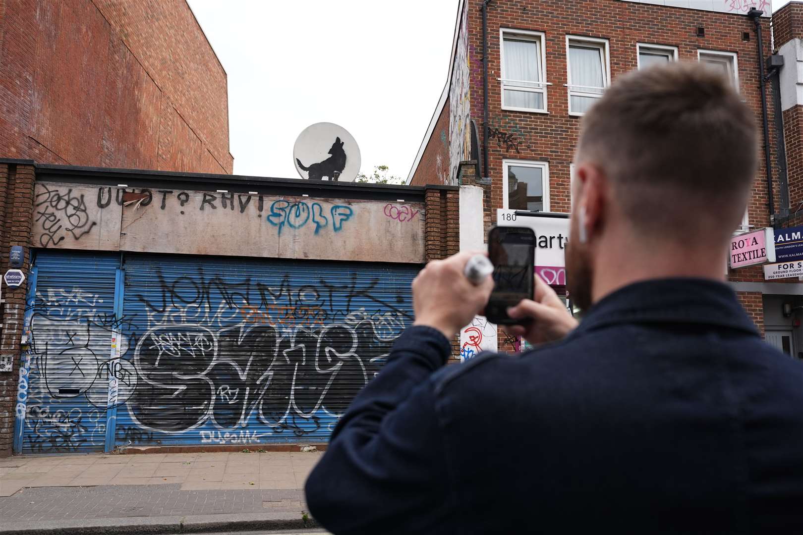 A man takes a picture of the new howling wolf Banksy in Peckham, south London (Jordan Pettitt/PA)