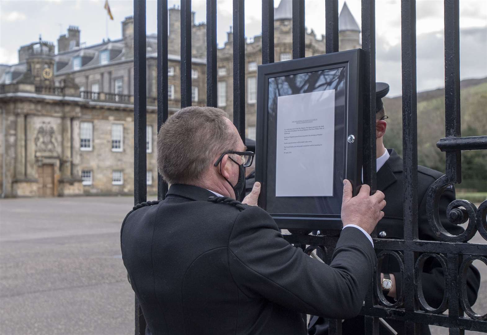 A member of staff attaches a notice to the gates of the Palace of Holyroodhouse in Edinburgh announcing the death of the Duke of Edinburgh (Lesley Martin/PA)