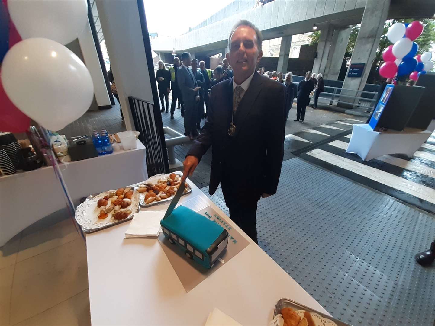 Cllr Derek Mortimer cuts a cake in the shape of a bus to mark the opening