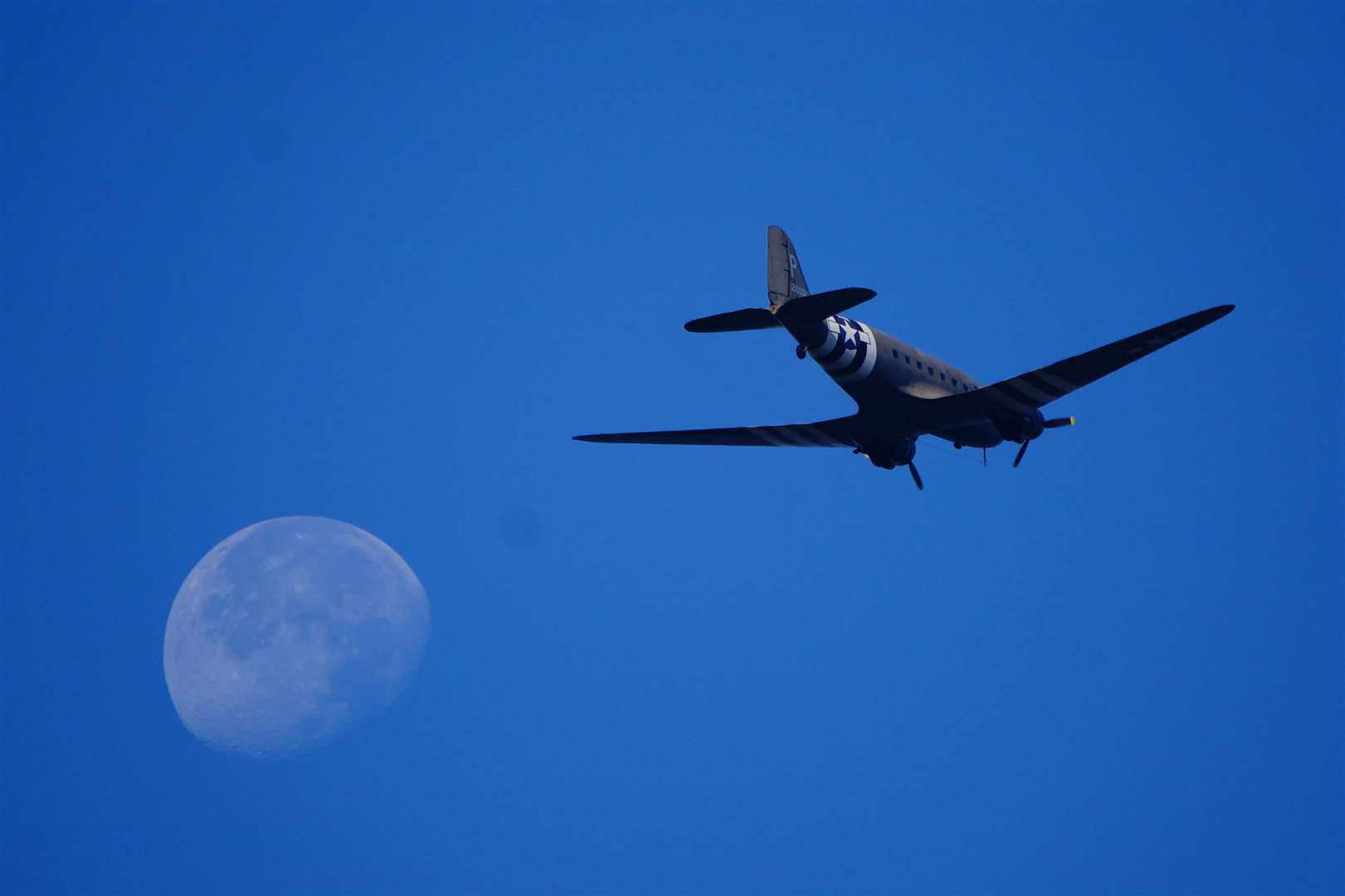 A US plane passes in front of the moon before paratroopers take the leap (Ben Birchall/PA)