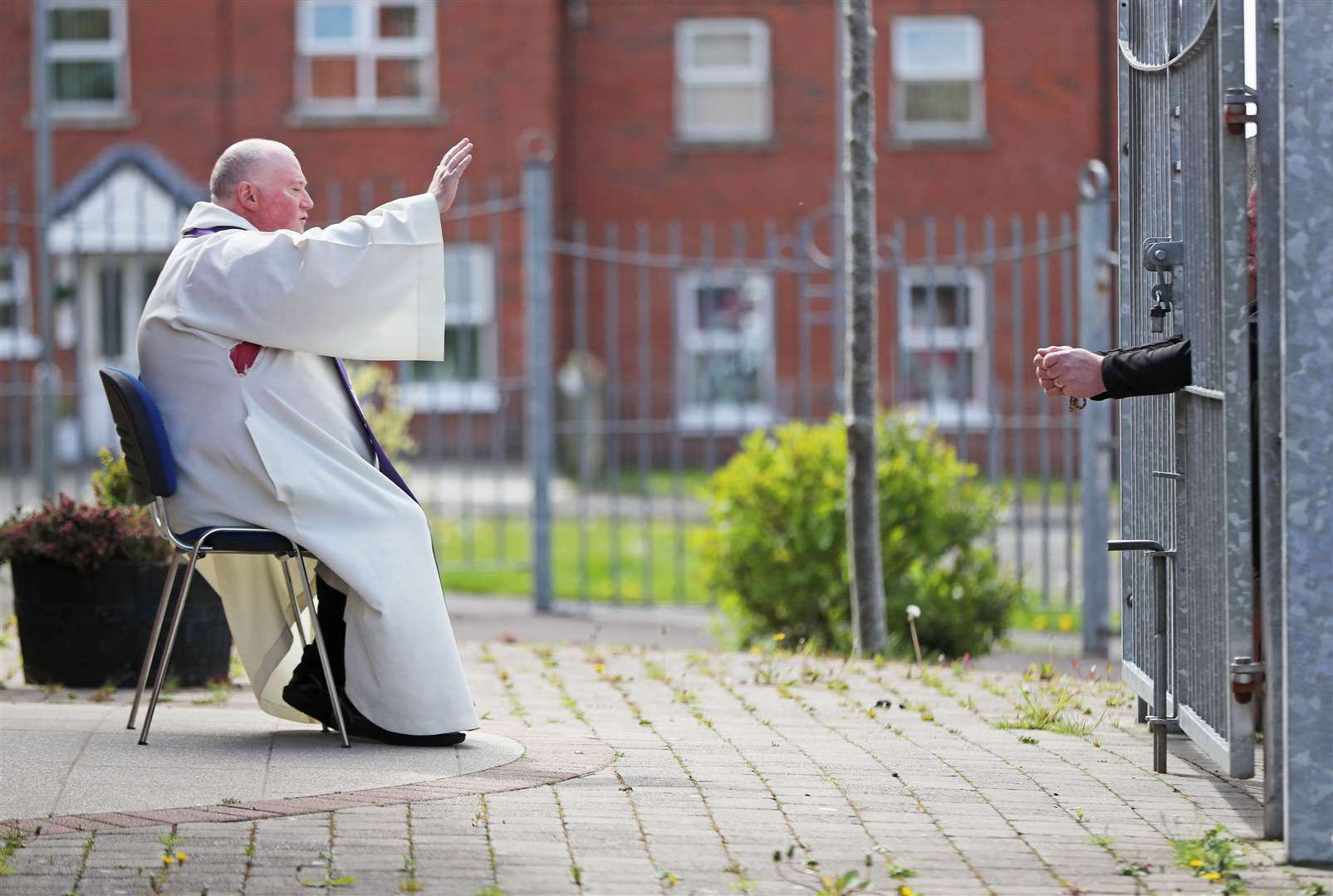 Father Paddy McCafferty resumes hearing confessions while observing social distancing though the locked gates of Corpus Christi Church in Ballymurphy (Niall Carson/PA)