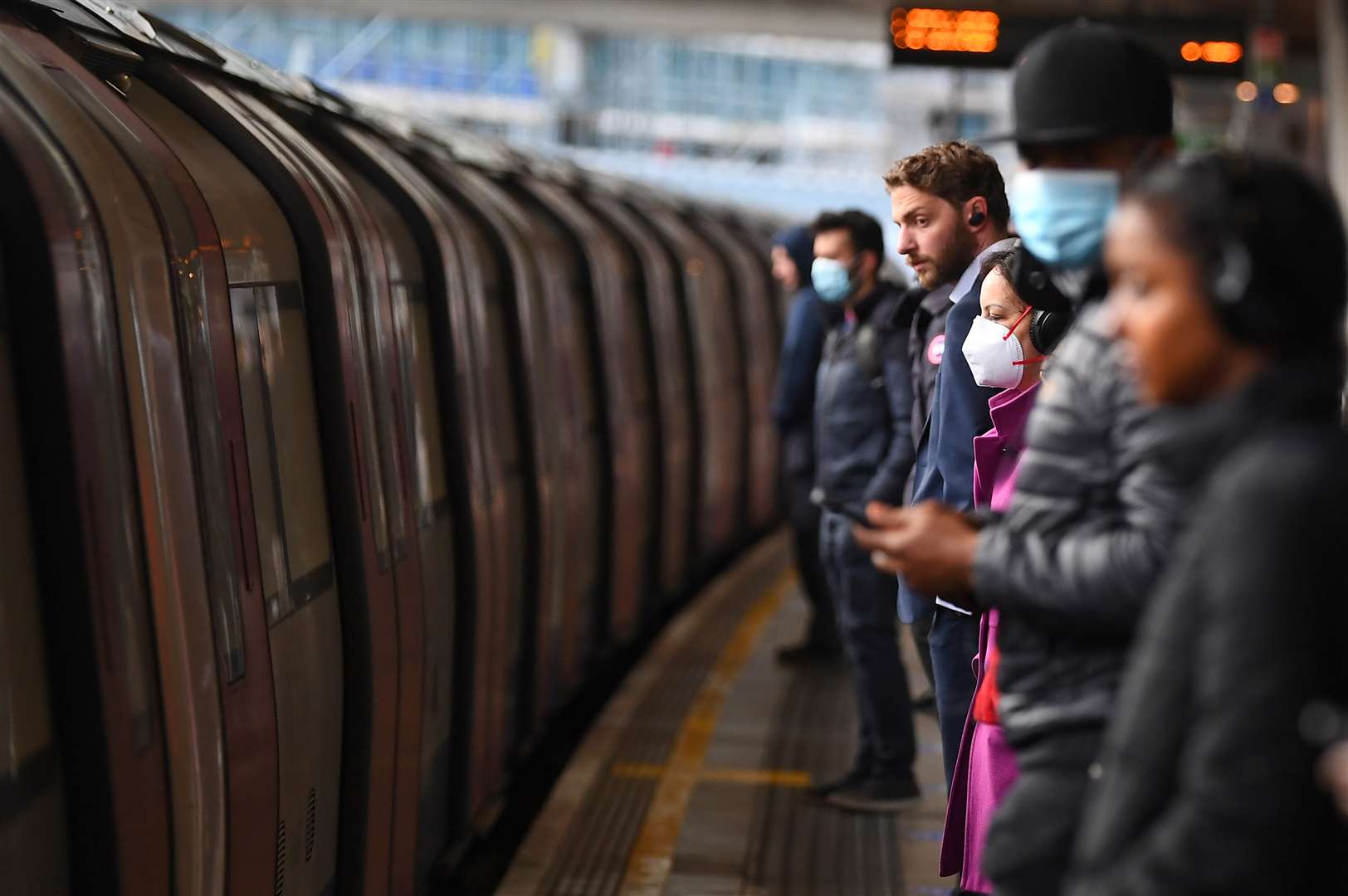 Passengers wear face masks and stand apart on a platform at Canning Town underground station (PA)