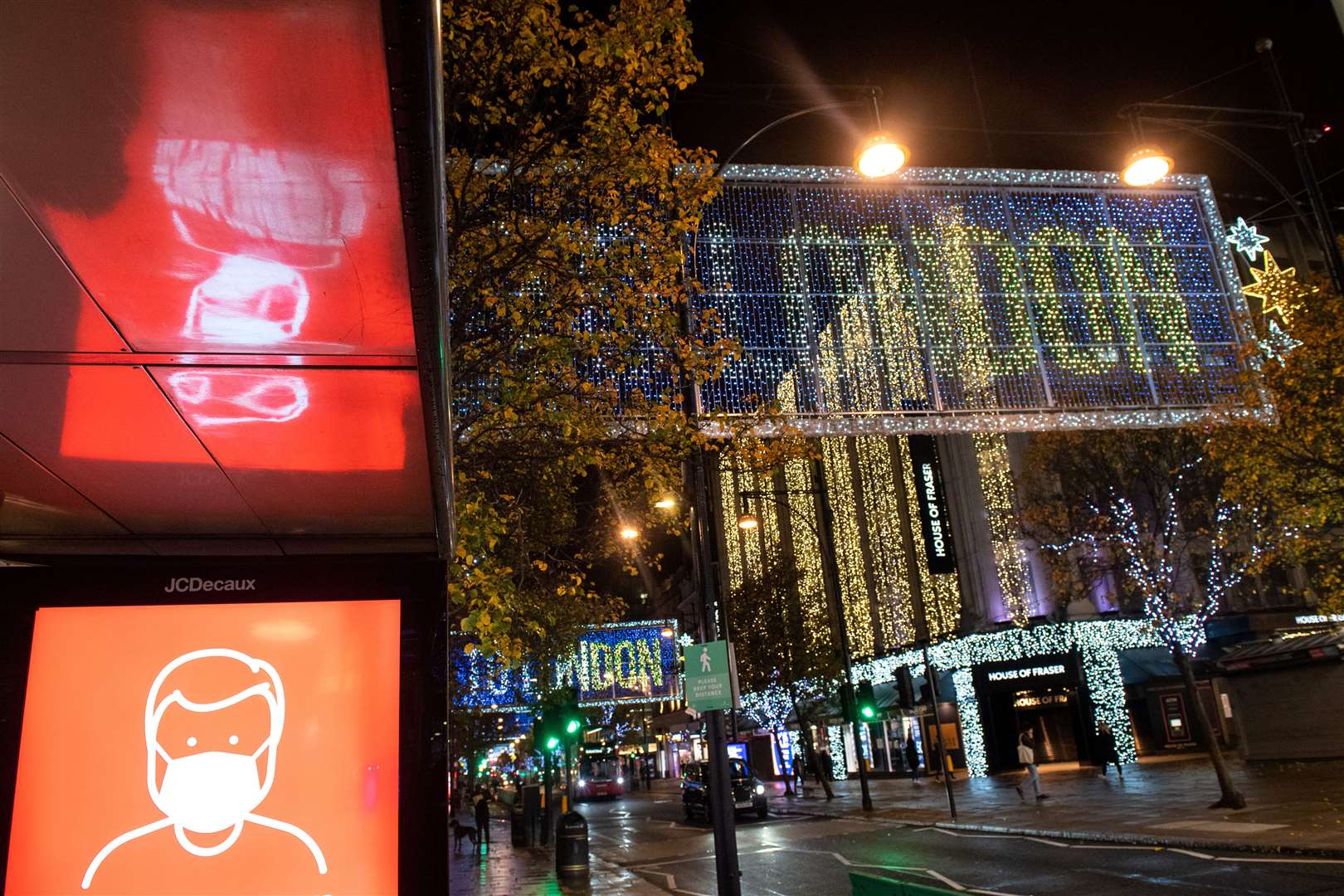 A screen advising the wearing of face masks is seen alongside Christmas lights on Oxford Street (Dominic Lipinski/PA)