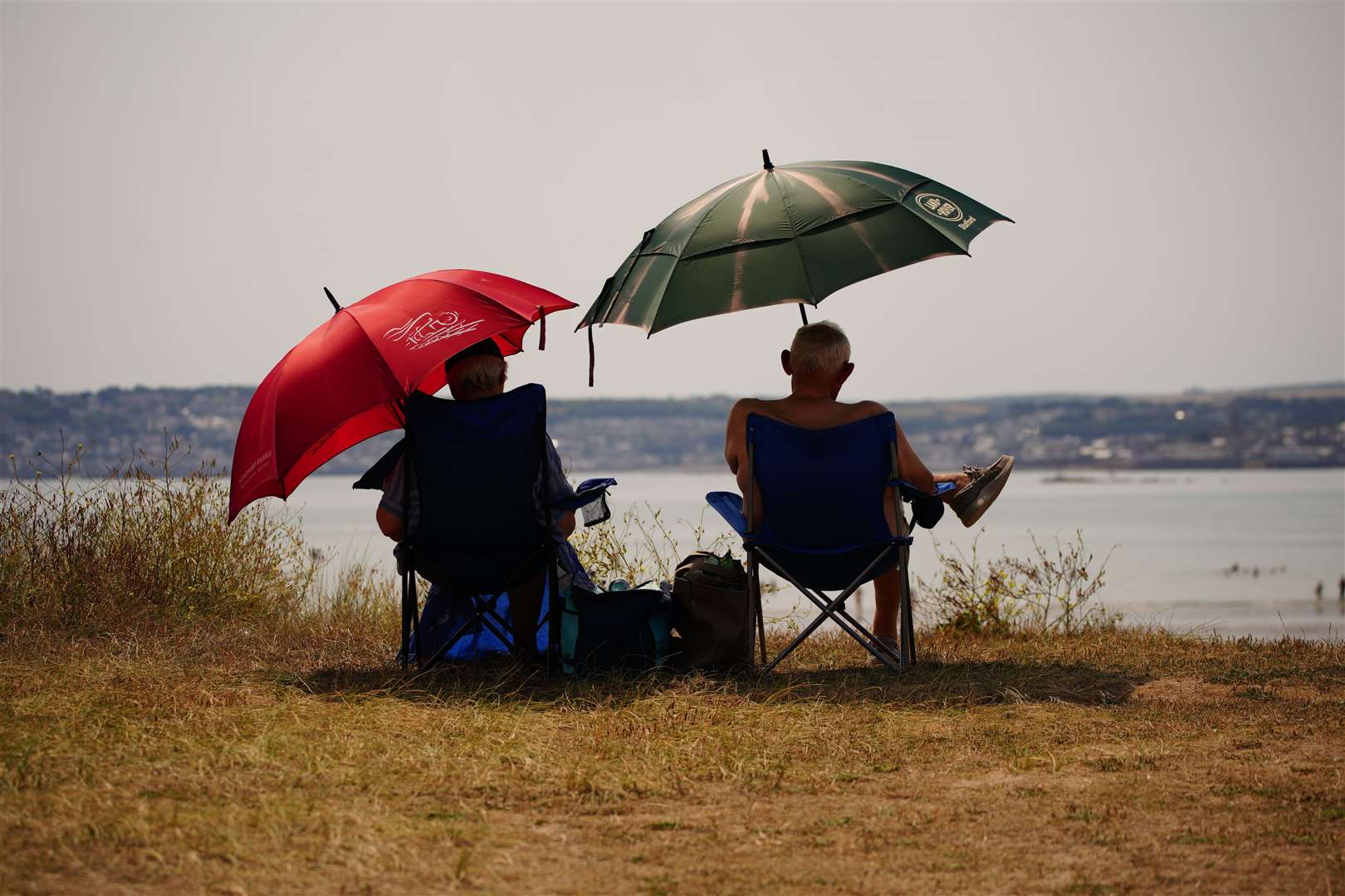 People sheltering under umbrellas from the sun in St Michael’s Bay in Cornwall (Ben Birchall/PA)