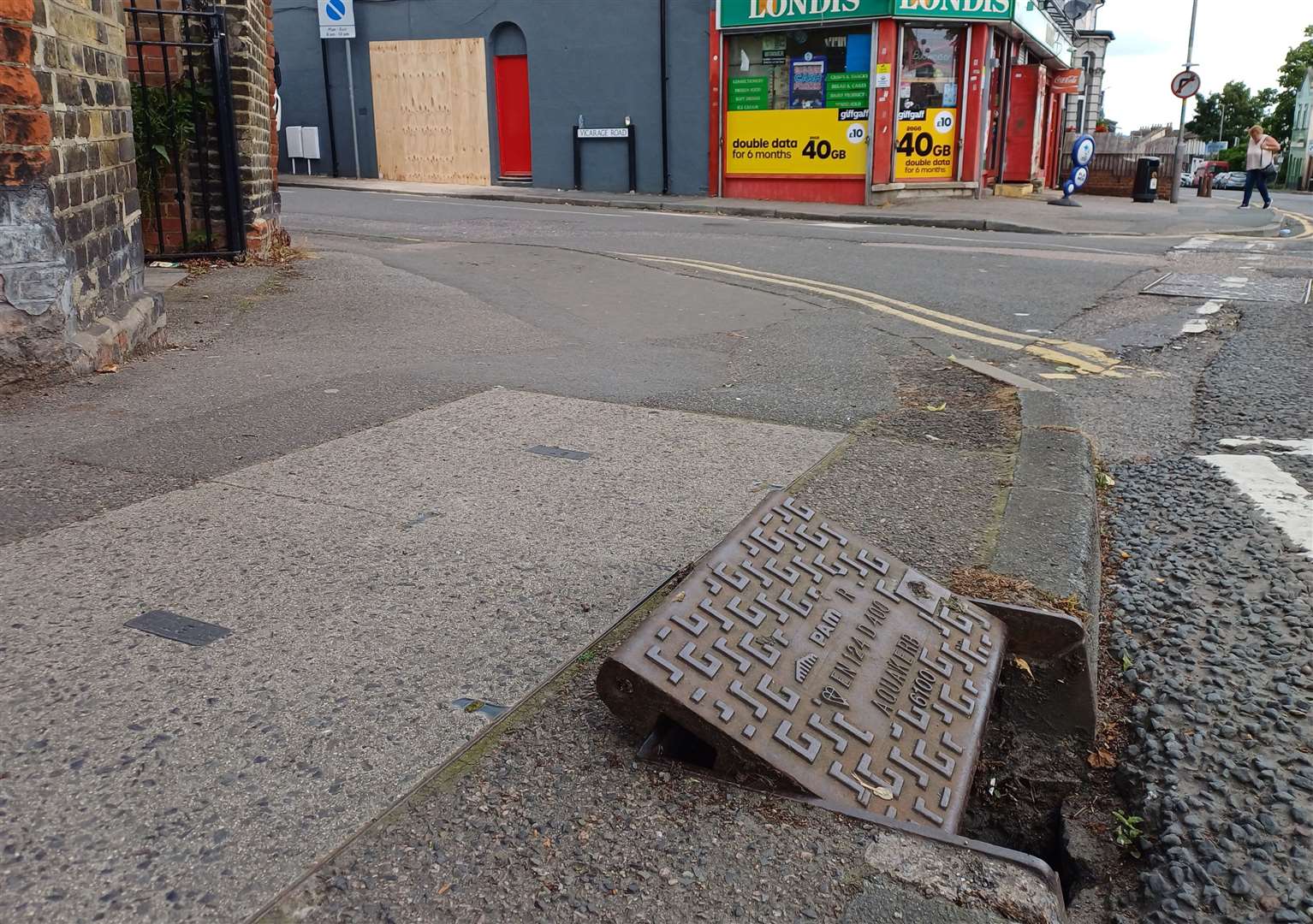 The Dislodged drain cover and the boarded up wall at the scene of the car crash in Vicarage Road, Gillingham