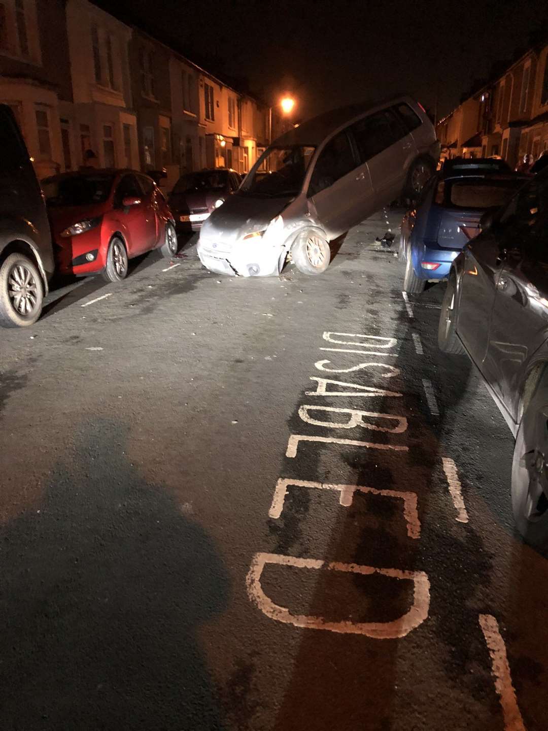 The damaged car on its roof after colliding with several parked vehicles