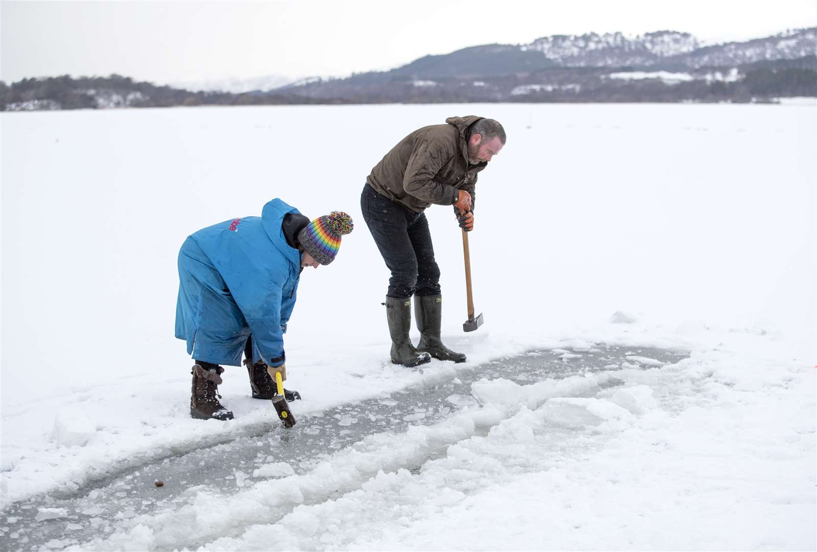 Al and Alice Goodridge use a sledgehammer and axe to create a channel in the ice in Loch Insh, in the Cairngorms National Park, for Alice to swim in (Jane Barlow/PA)