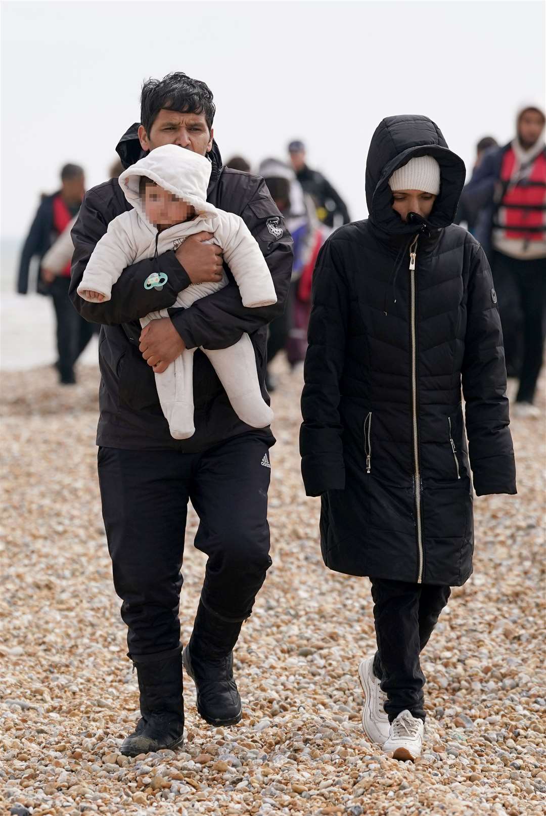 A group of people thought to be migrants, including young children, walk up the beach in Dungeness (Gareth Fuller/PA)