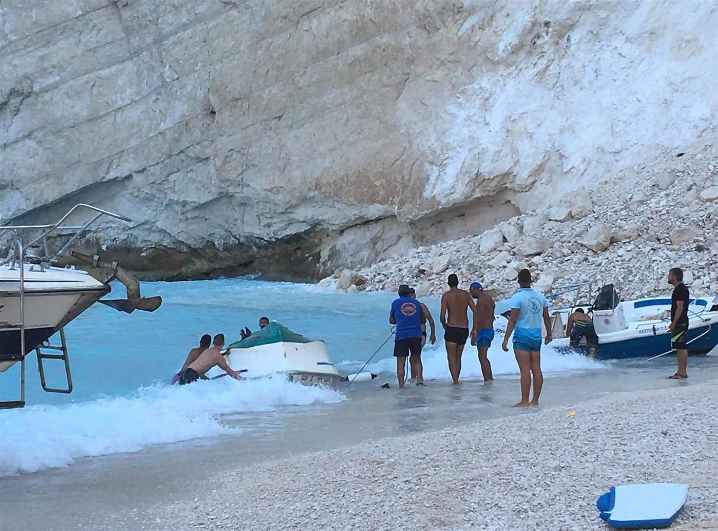 People attempt to right a boat after the weight of the cliff fall caused it to capsize