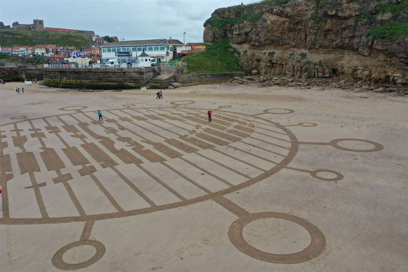 People walk across the giant piece of sand art on the beach at Whitby (Richard McCarthy/PA)