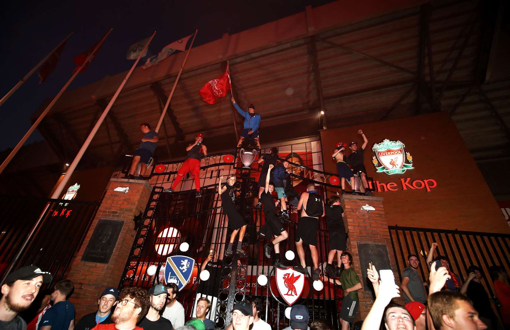 Liverpool fans celebrate on top of the gates outside Anfield (Martin Rickett/PA)