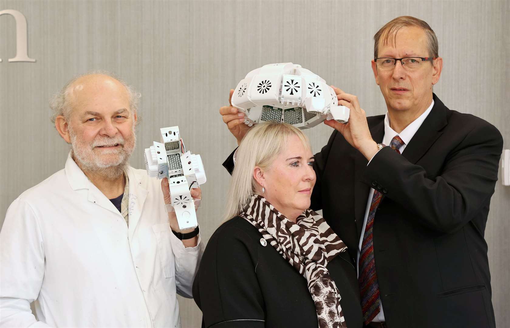 Dr Paul Chazot, holds a preclinical PBM-T test device while Dr Gordon Dougal fits the infrared light therapy helmet to Tracy Sloan (Durham University/PA)