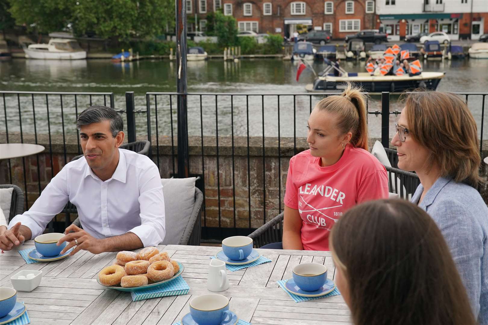 Rishi Sunak speaking to rowing club members as Liberal Democrat supporters wave placards from a boat behind him (Jonathan Brady/PA)