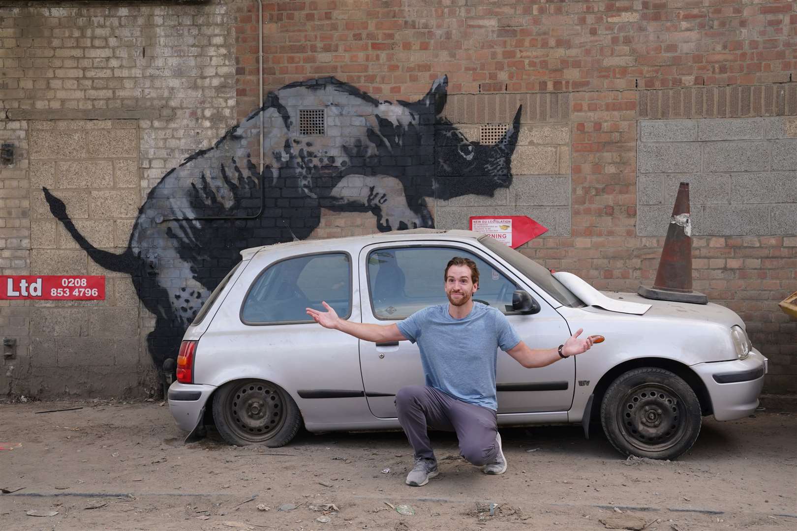 A man poses for a photograph by a new artwork unveiled by Banksy, depicting a rhinoceros (Lucy North/PA)