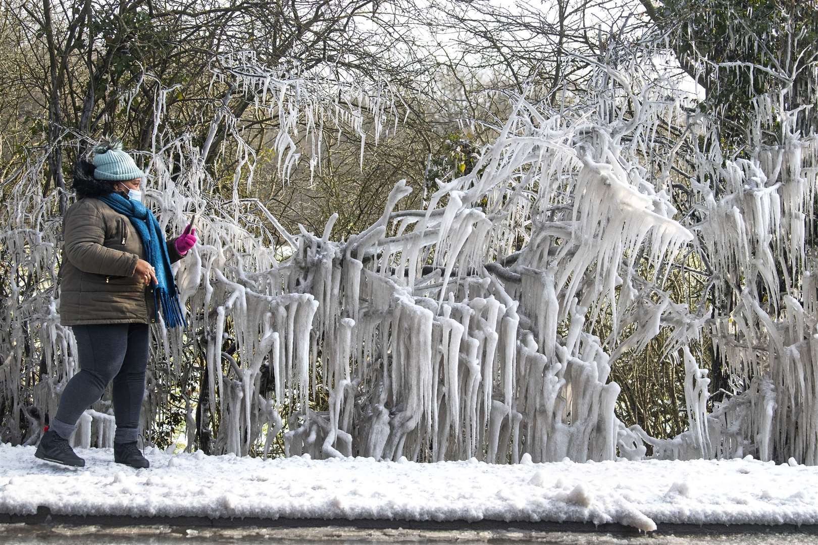 A woman takes a photograph of large icicles forming in Epping Forest (Victoria Jones/PA)