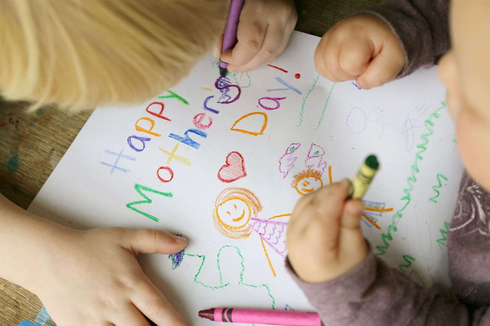 Two young children colouring a card with crayons specially for Mother's Day