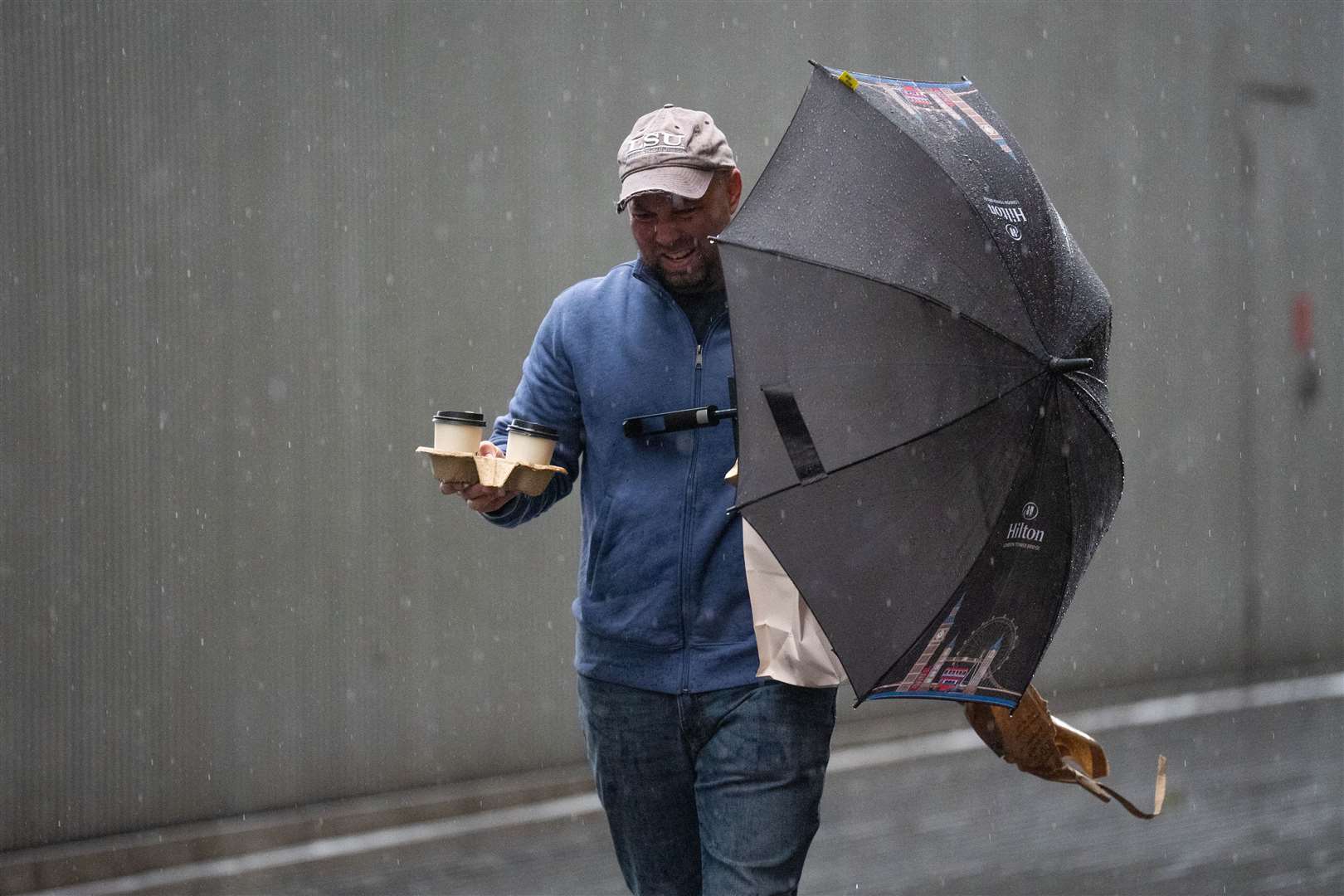 Juggling takeaway coffee and an umbrella proved a difficult task for this man near Tower Bridge in London (James Manning/PA)