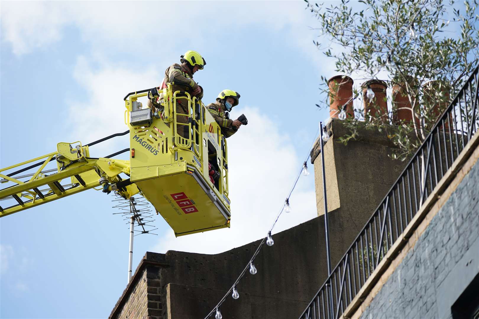 Firefighters in a crane are seen on the top of the pub pouring water into the air vents. (Yui Mok/PA)