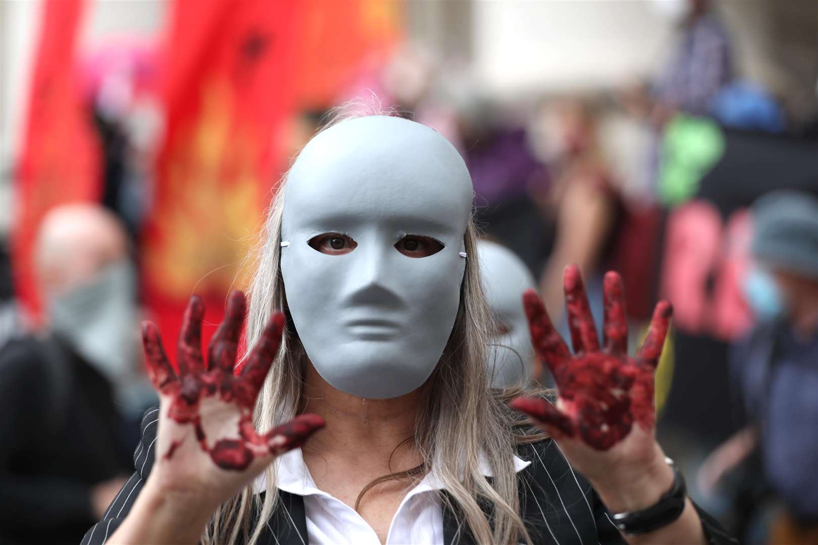 A masked protester, hands covered with fake blood, stands outside the Bank of England (Luciana Guerra/PA)