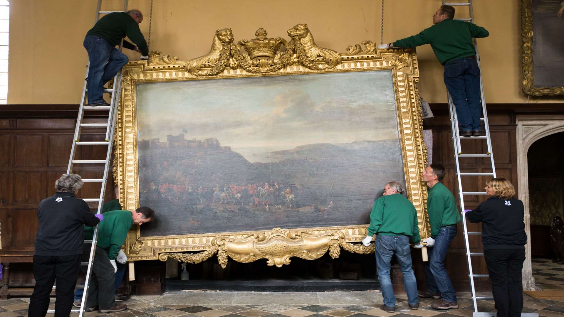 The Knole House conservation team work together to carefully remove John Wootton’s painting from above the fireplace in the Great Hall