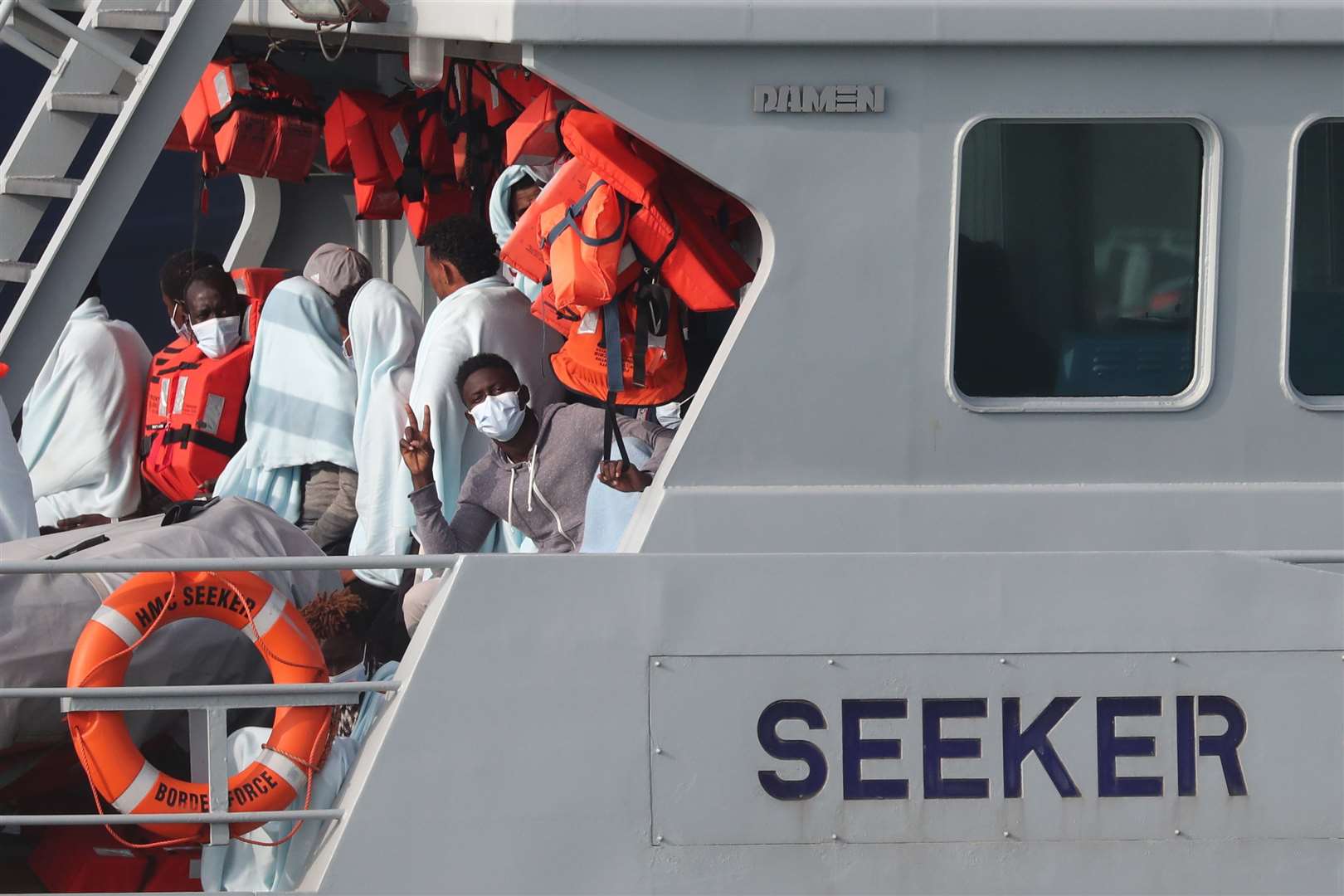 One of a group of people, thought to be migrants, makes a victory gesture on the deck of HMC Seeker (Gareth Fuller/PA)