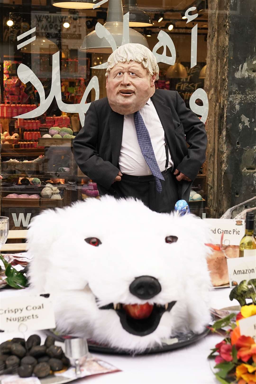 An actor dressed in a mask depicting Prime Minister Boris Johnson dined at a banquet of environmental and climate degradation during a performance on Buchanan Street (Danny Lawson/PA)