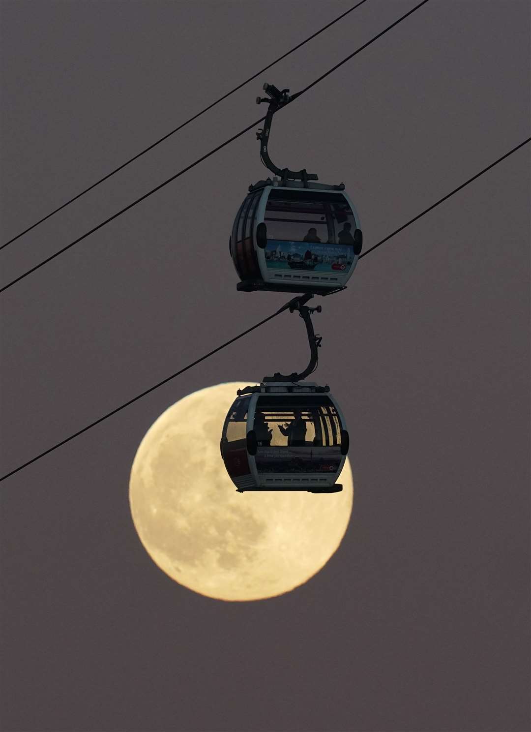 Cable cars pass in front of the moon as they cross the River Thames in London (Yui Mok/PA)