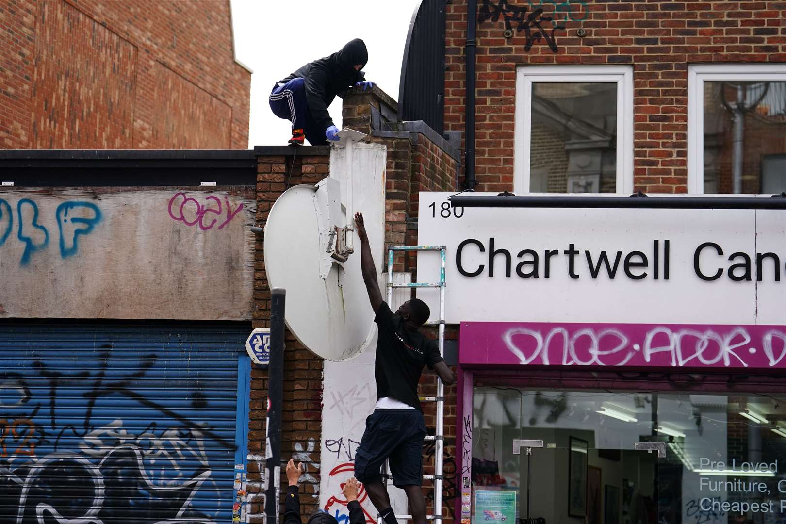 People remove a new artwork by Banksy, a howling wolf painted on a satellite dish (Jordan Pettitt/PA)