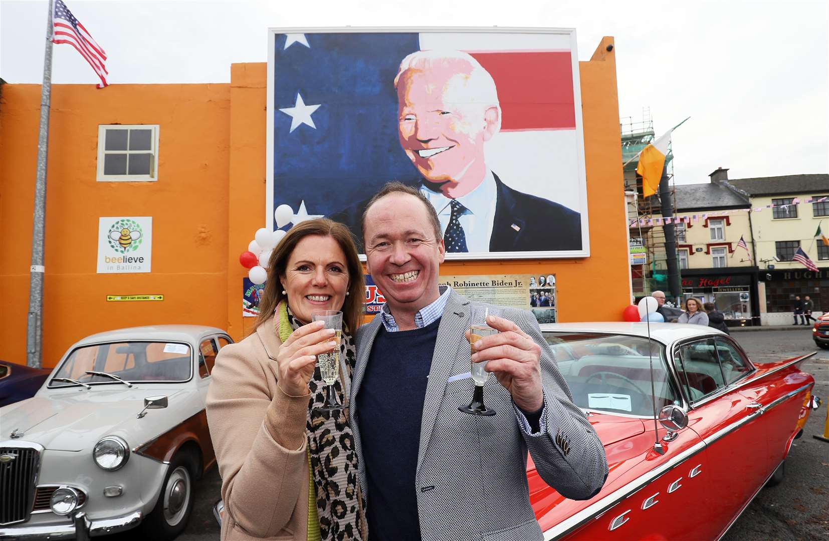 Joe Blewitt, a cousin of Mr Biden, and his wife Deirdre celebrating in front of a mural of Mr Biden in his ancestral home of Ballina, Co. Mayo, Ireland (Brian Lawless/PA)