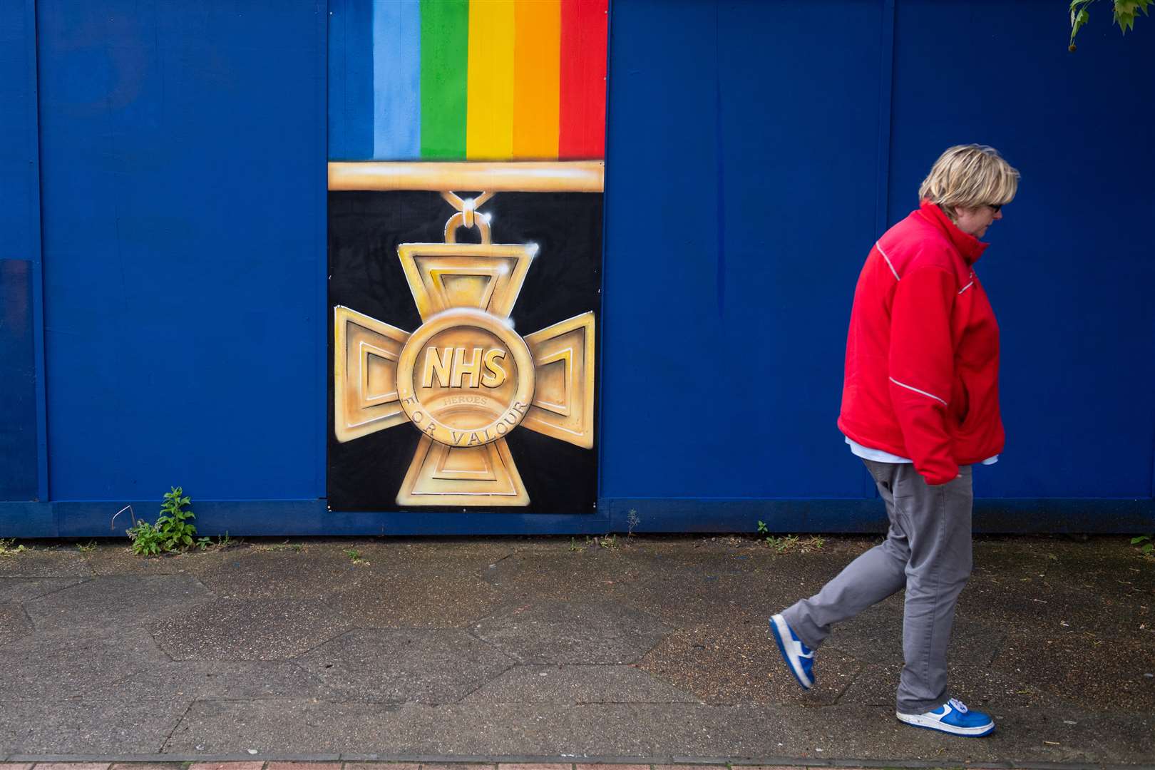 A woman passes a mural showing an NHS medal in south London (Dominic Lipinski/PA)