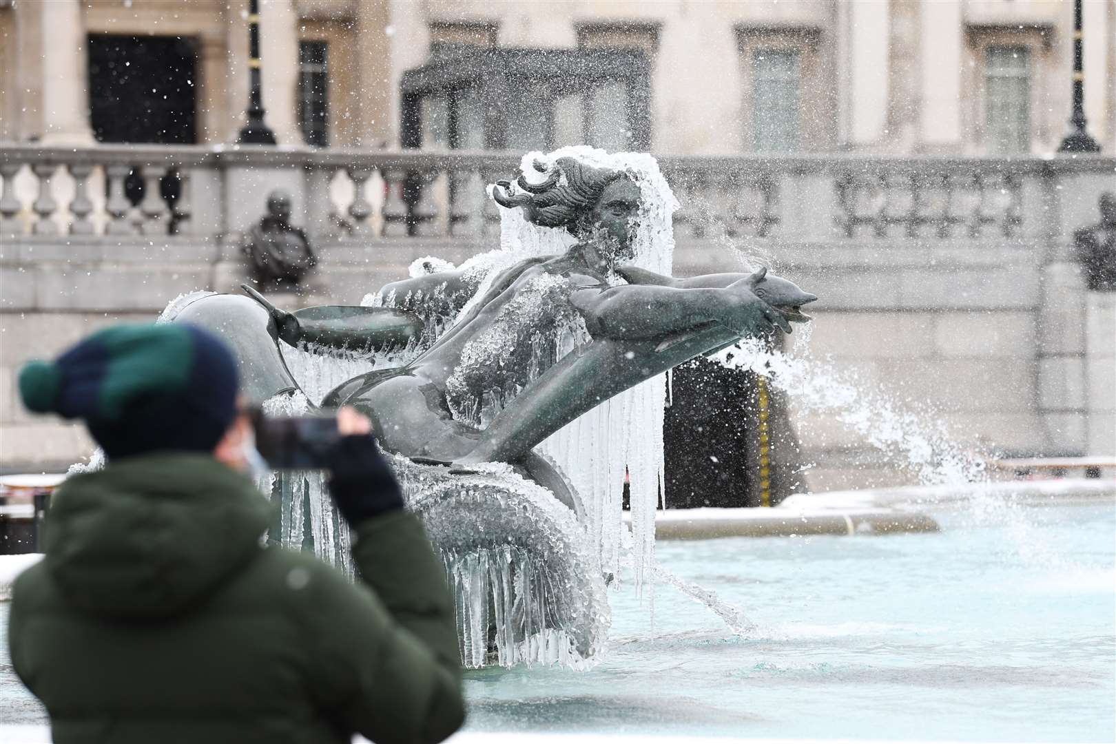 A man takes a photo of an ice-covered mermaid statue in Trafalgar Square, London (Stefan Rousseau/PA)