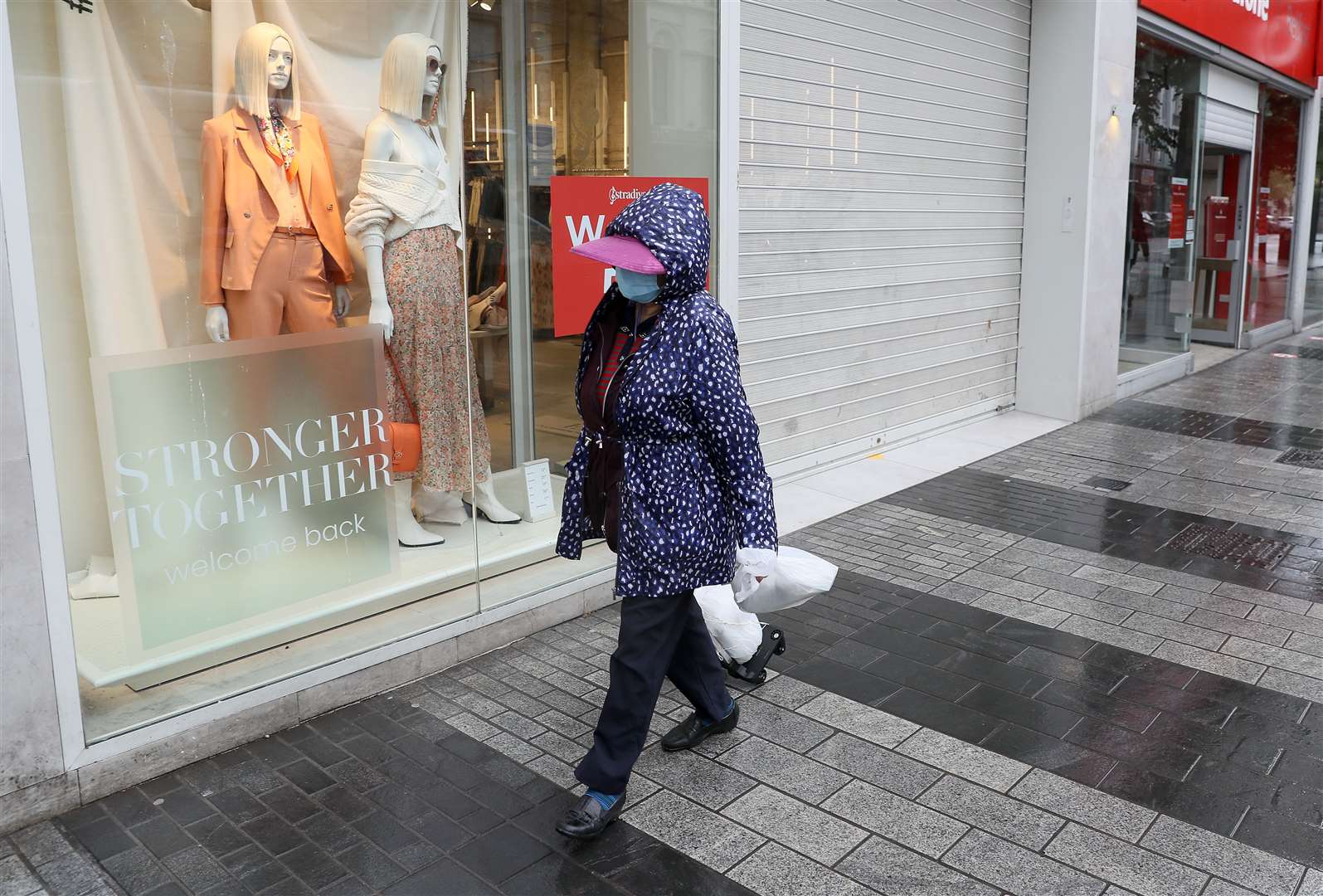 A woman wearing a face covering passes a shop window in Belfast (Brian Lawless/PA)